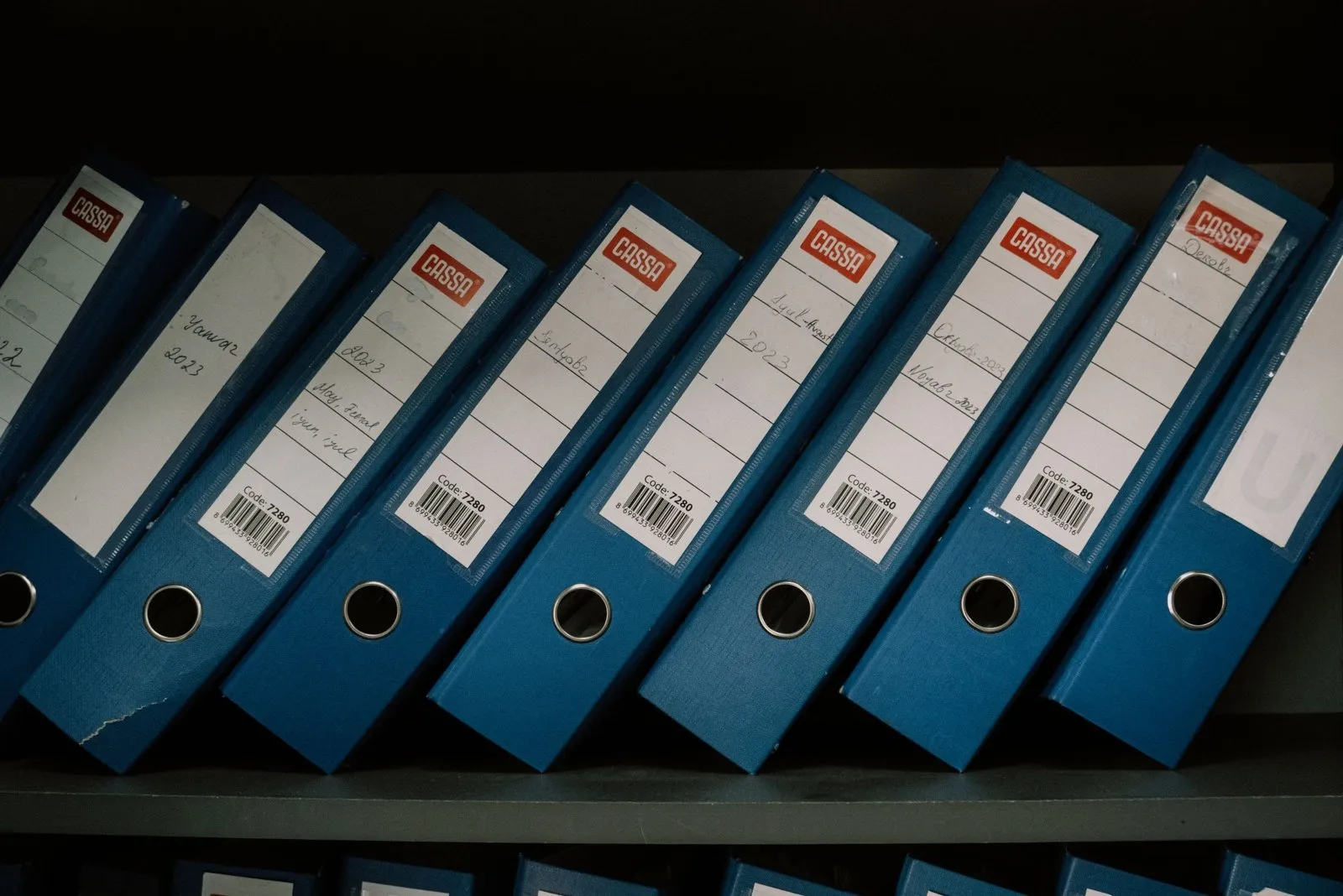 Bureau clair avec piles de relevés bancaires, classeur, calculatrice et étiquettes de tri colorées.